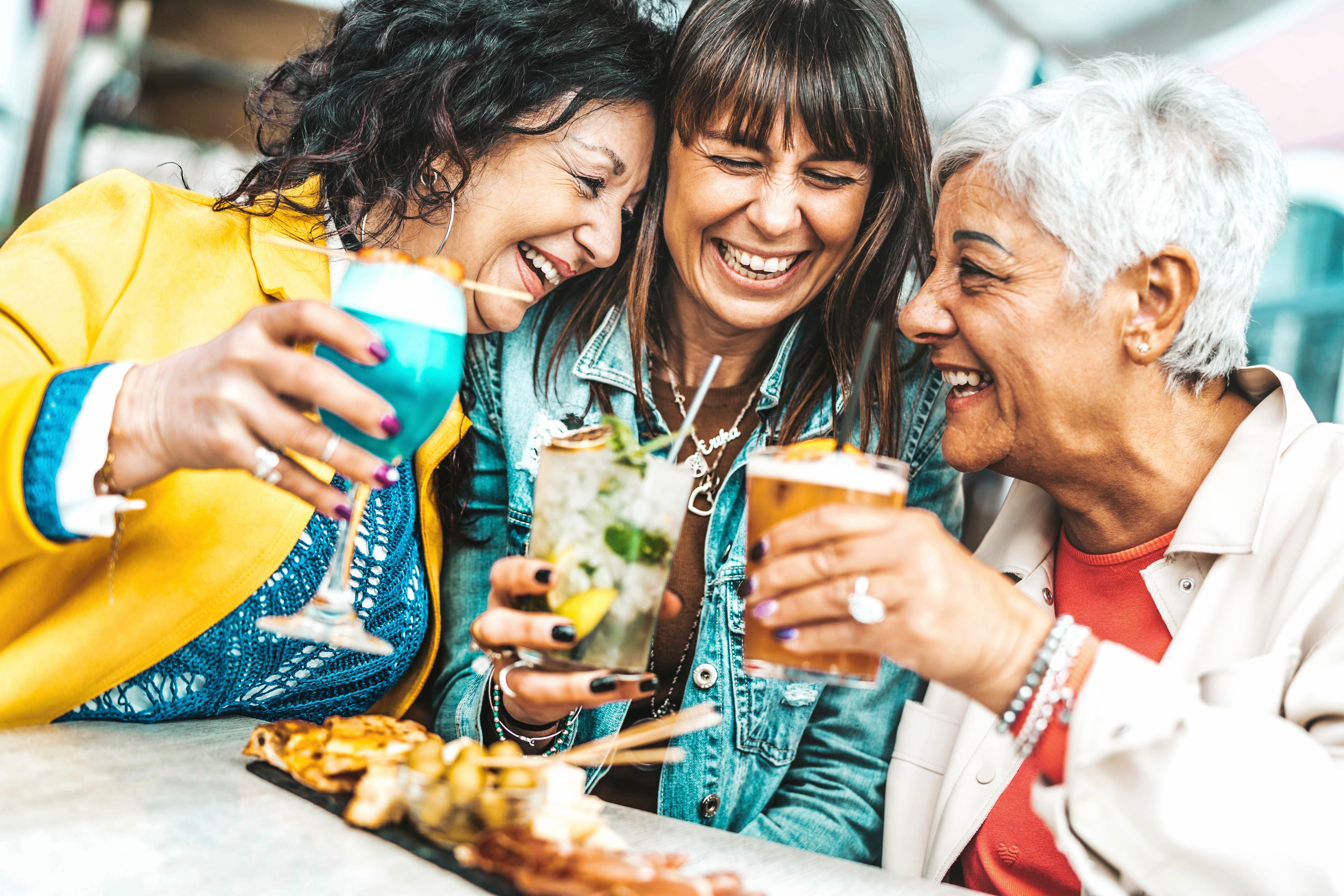 Happy senior women drinking cocktail glasses sitting at bar table