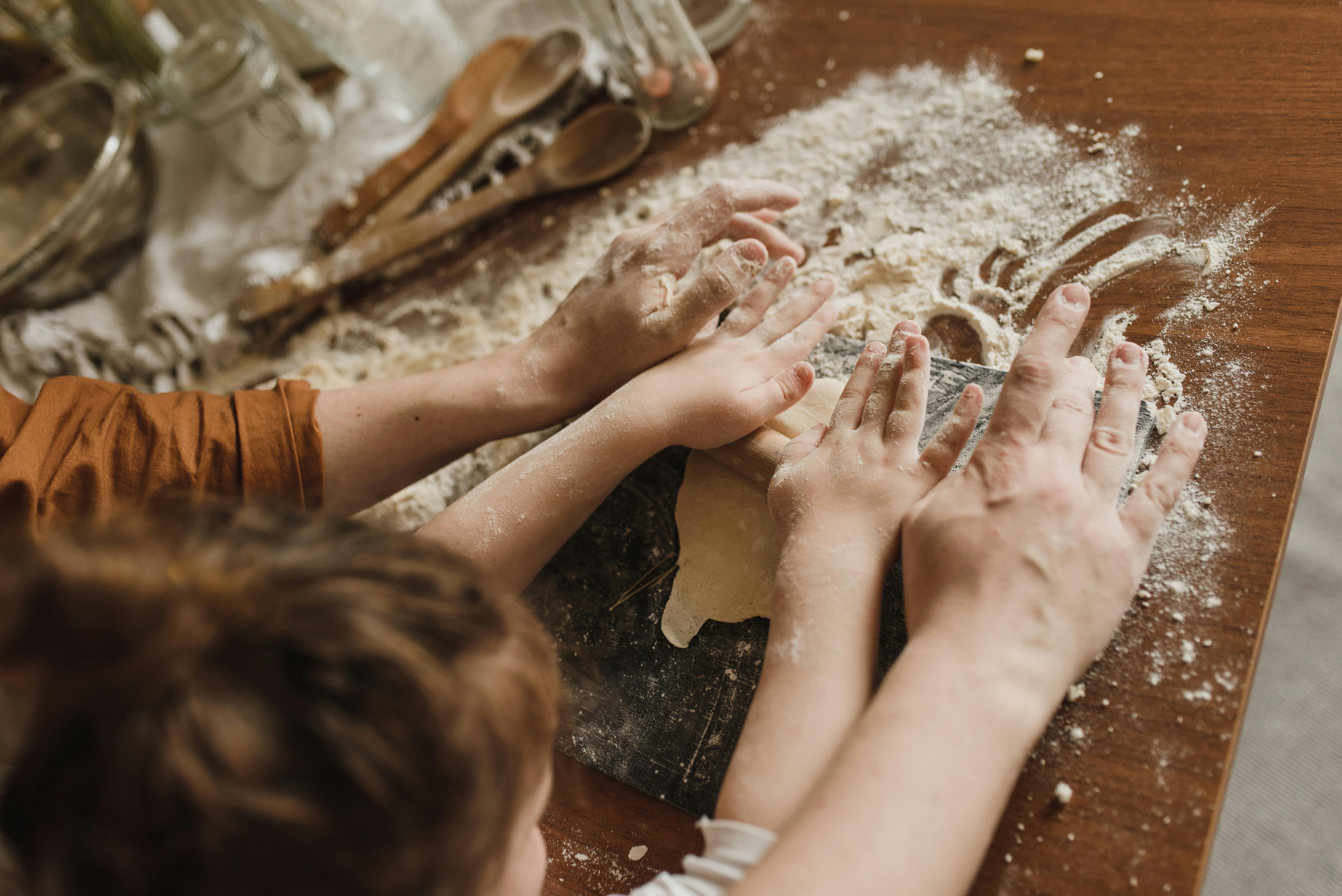 Adult and child's hands rolling dough on a floured tabletop
